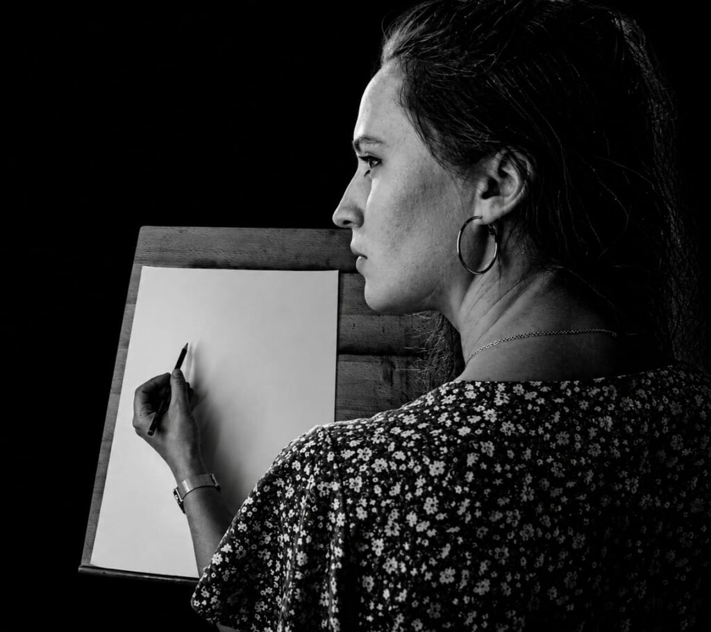 Elia à sa table de travail, le crayon posé sur un dessin en cours